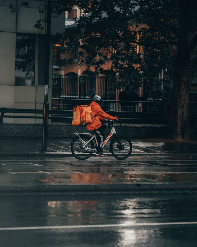 Repartidor en bicicleta con mochila de reparto sobre pavimento mojado, 10 claves infraestructura perfecta bicicletas ciudad