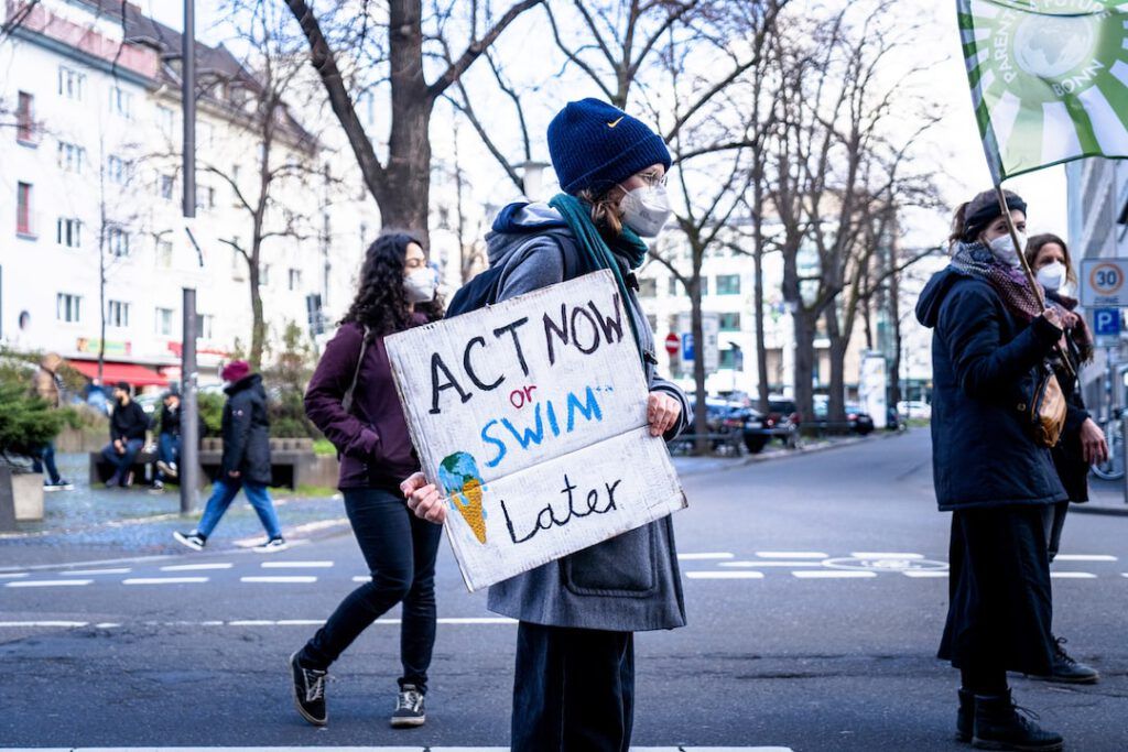 Manifestantes en la calle con mascarillas sostienen un cartel 'Act Now or Swim Later' que simboliza 10 consejos adaptarnos cambio climatico futuro.