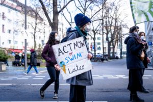 Manifestantes en la calle con mascarillas sostienen un cartel 'Act Now or Swim Later' que simboliza 10 consejos adaptarnos cambio climatico futuro.