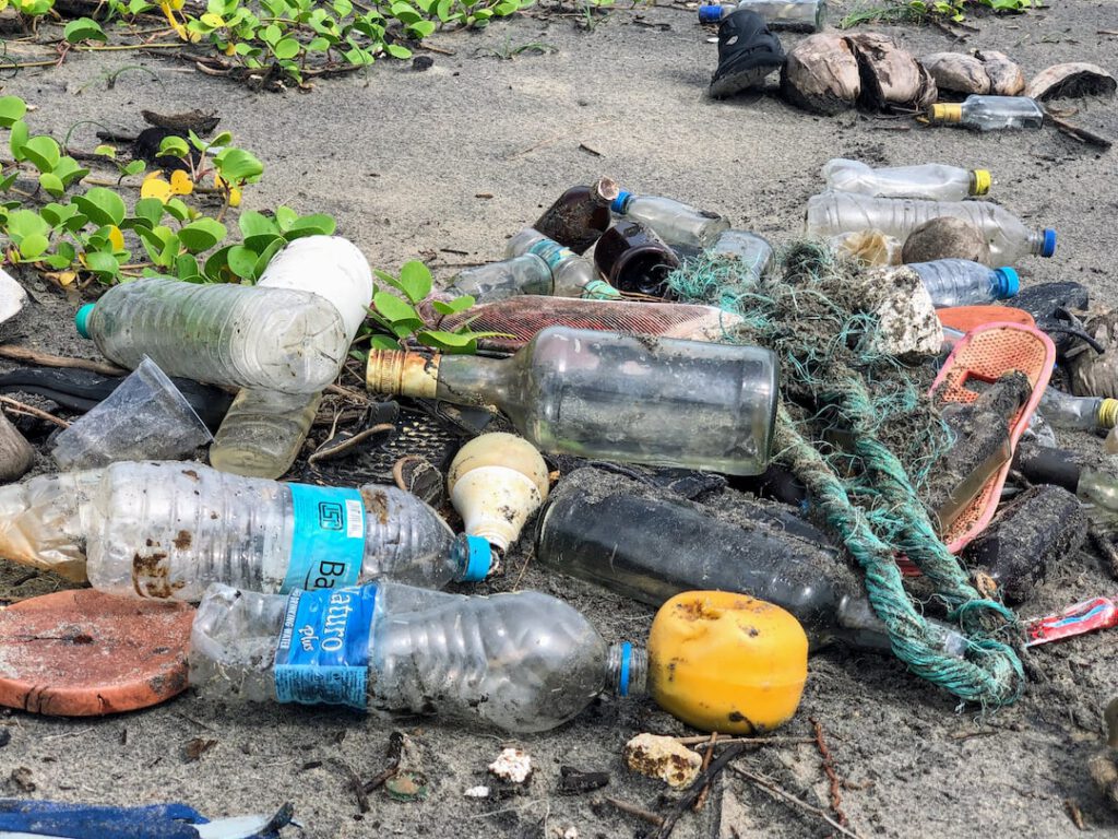 Playa con botellas de plástico y vidrio, cuerdas, chanclas y otros residuos dispersos que exigen 10 medidas reducir contaminacion quimica hogar industria