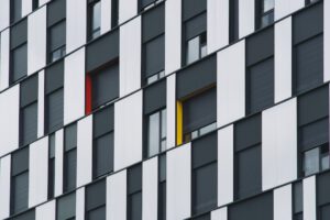 Fachada de edificio con paneles verticales blancos y negros, ventanas con persianas y acentos rojo y amarillo, 10 soluciones abonos organicos plantas
