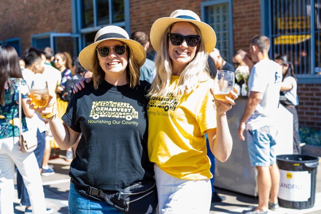 Dos personas sonrientes en un evento al aire libre con bebidas y un contenedor de residuos, mostrando oportunidades para 5 formas promover economia circular plastico