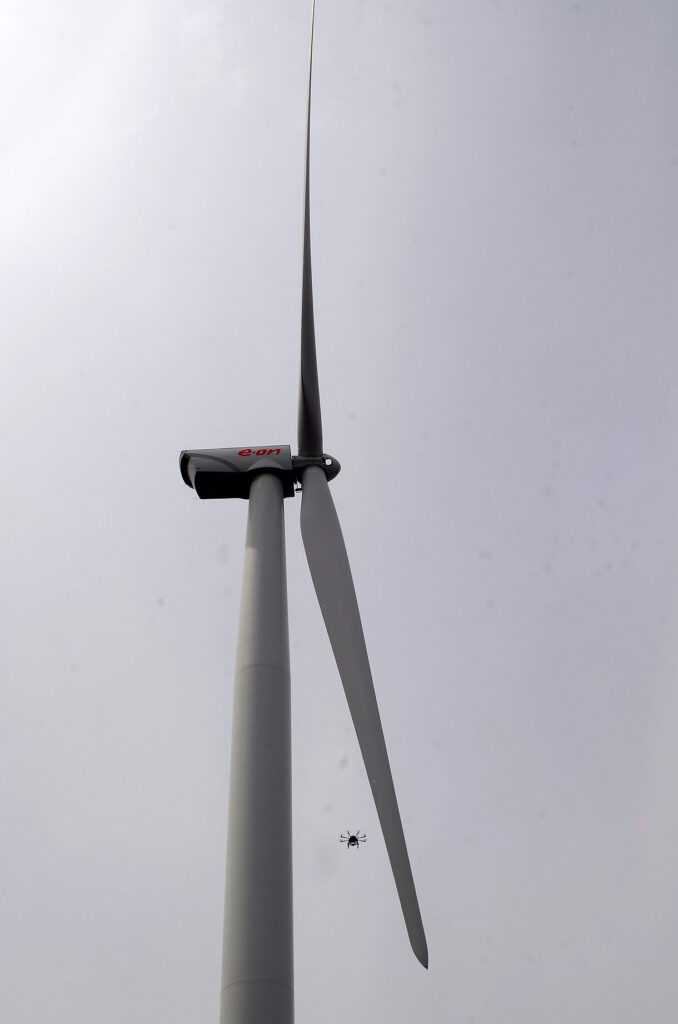 Aerogenerador alto visto desde la base con un dron de inspección cerca de la pala