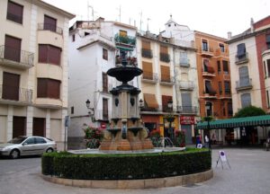 Fuente ornamental en plaza con agua limpia 1 rodeada de edificios y macetas