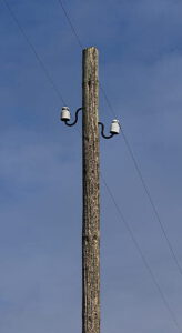 Poste de madera con aisladores y cables eléctricos contra un cielo azul, recurso visual para agua reutilizada