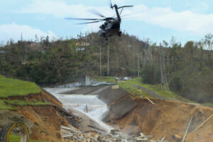 Helicóptero sobre una estructura colapsada con agua fluyendo, mostrando la urgencia de garantizar agua segura.