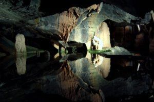 Caverna iluminada con formaciones rocosas y espejo de agua que muestra agua subterranea 1.