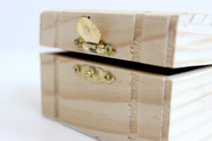 Caja de madera clara con bisagra y cierre dorado para almacenamiento seguro de pequeños objetos.