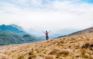 Persona con brazos abiertos en una colina mirando un valle montañoso, aplicar abonos organicos efectiva mejora salud plantas