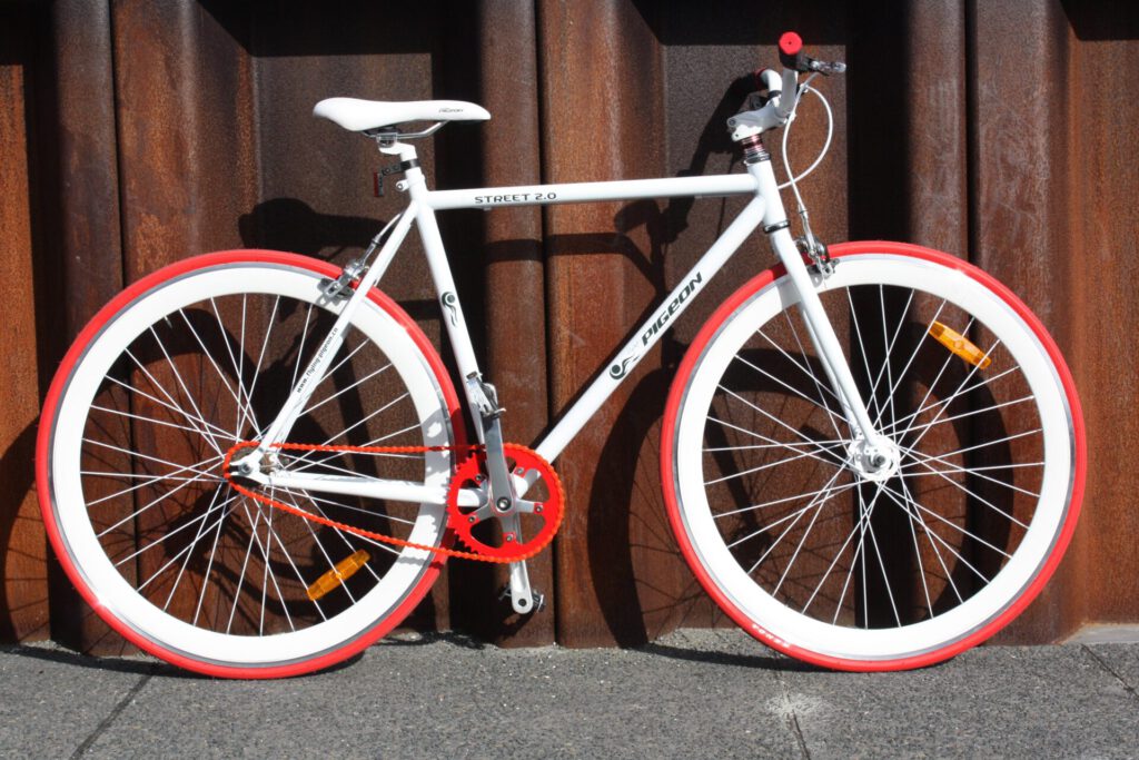 Bicicletas de estilo urbano blanco y rojo con cuadro fijo apoyadas en una pared metálica