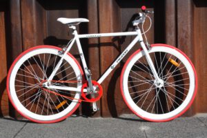 Bicicletas de estilo urbano blanco y rojo con cuadro fijo apoyadas en una pared metálica