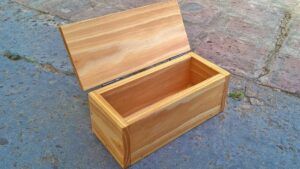 Caja madera rectangular abierta de madera clara con tapa abatible y bisagras visibles