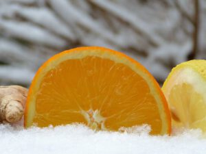 Rodajas de naranja y limón con jengibre sobre nieve que evocan prevención frente al clima enfermedades.