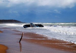 Barco varado en una costa inundada con olas rompiendo y cielo nublado.