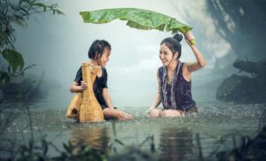 Dos personas sentadas en agua bajo la lluvia protegiéndose con una hoja grande mientras se plantea cuanto tanque captar almacenar agua lluvia.