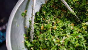 Ensalada de kale picada con semillas y pasas en un bol metálico, descubre beneficios agricultura urbana periurbana