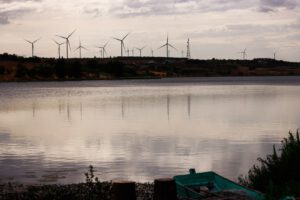 Embalse tranquilo con barca en primer plano y turbinas eólicas en el horizonte, descubre beneficios energia hidroelectrica