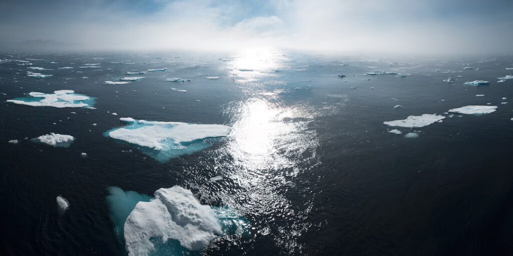 Placas de hielo fragmentadas flotando en el océano con el sol reflejado, descubre causas aumento temperaturas.