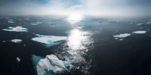 Placas de hielo fragmentadas flotando en el océano con el sol reflejado, descubre causas aumento temperaturas.
