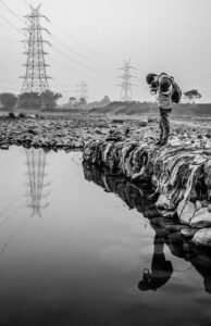 Persona con cámara en la orilla observando el agua y su reflejo, descubre fuentes contaminacion agua