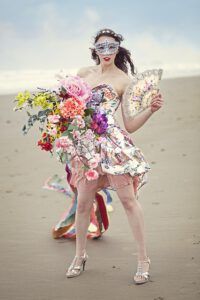 Mujer con máscara, vestido floral, abanico y gran ramo de flores en la playa descubre poder abonos organicos huerto