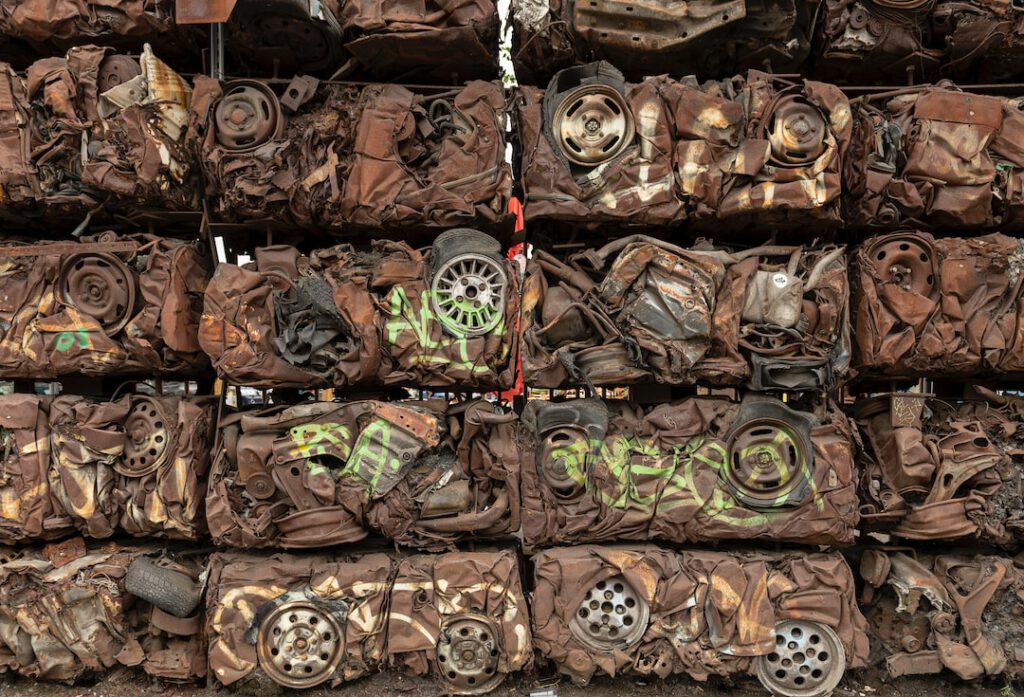 Pilas apiladas de carrocerías compactadas y ruedas oxidadas en un depósito de chatarra, descubre recoleccion metales reciclaje.