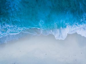 Vista aérea de la costa con olas rompiendo sobre arena que muestra diferencias energia olas mareas impacto medio ambiente.