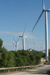 Aerogeneradores blancos sobre colinas arboladas junto a un camino bajo cielo azul, drenaje sostenible 1