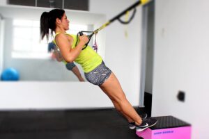 Mujer realizando ejercicio de suspensión con correas TRX trabajando espalda y core.