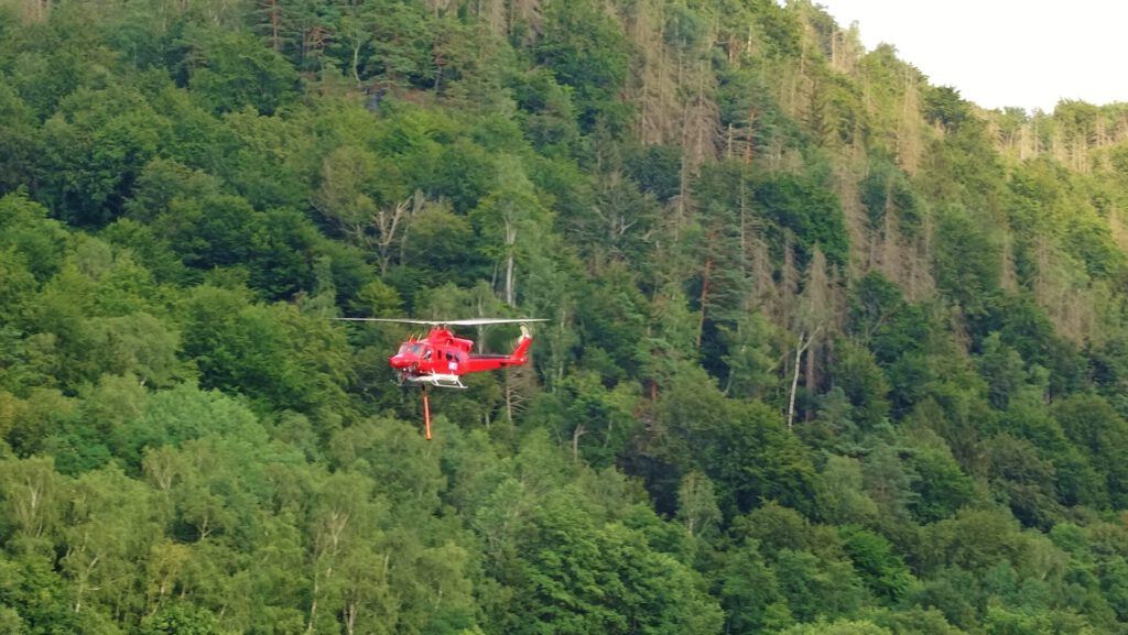 Helicóptero rojo sobre un bosque con equipo de extincion en labores de combate