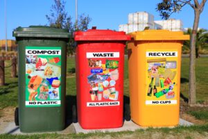 Tres contenedores de compost, residuos y reciclaje alineados en un parque, fomentando conciencia publica participacion reciclaje residuos electronicos