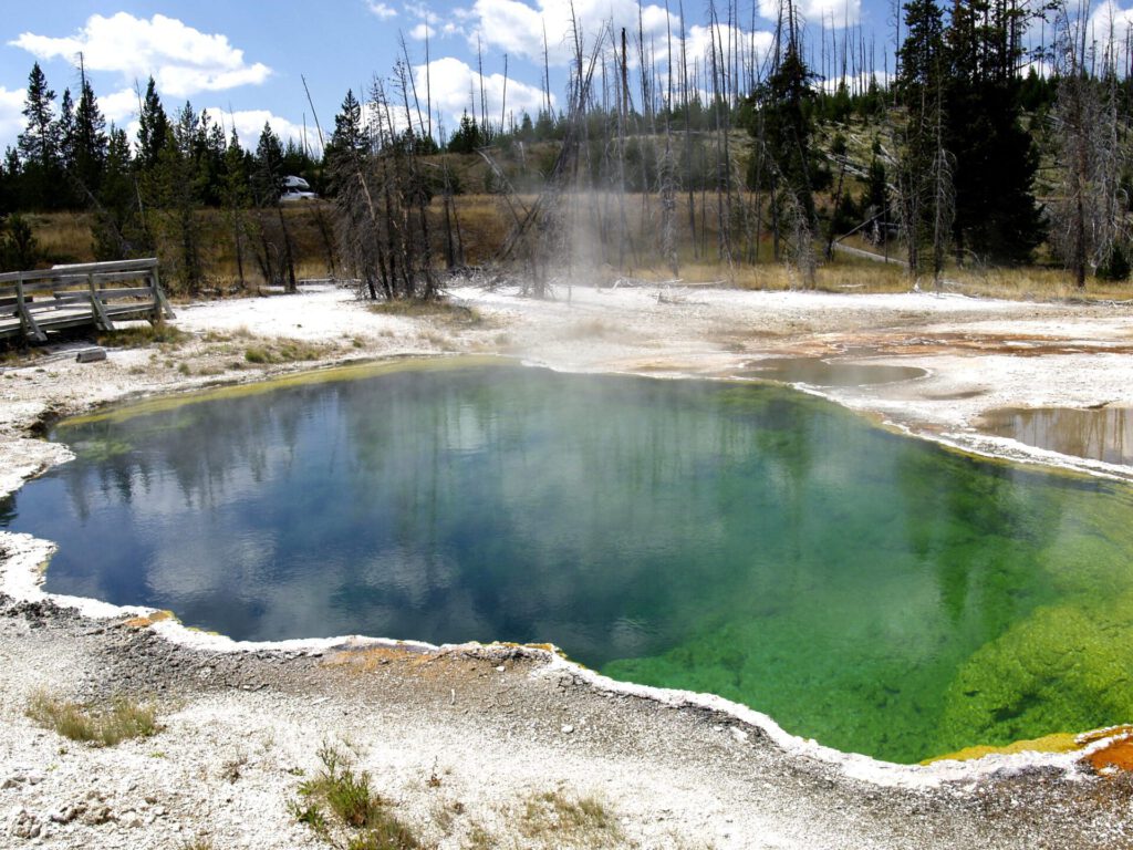 Piscina termal de color verdeazul con vapor y depósitos minerales, ejemplo de geotermia natural.