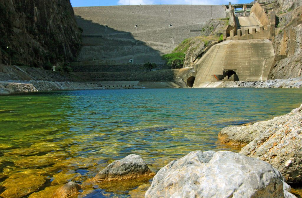 Vista frontal de una hidroelectrica con embalse y muros de presa, agua clara en primer plano.