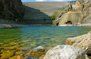 Vista frontal de una hidroelectrica con embalse y muros de presa, agua clara en primer plano.