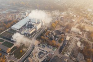 Fábrica emitiendo grandes columnas de humo sobre áreas urbanas que ilustran las impactantes consecuencias aumento temperaturas