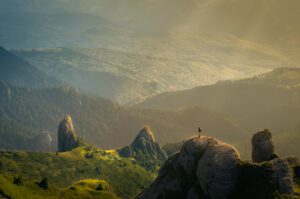 Persona en un risco observando valles y crestas verdes al amanecer, evocando impacto actividades humanas ecosistemas terrestres marinos