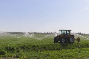 Tractor junto a aspersores en un campo verde, representando investigaciones cultivos cobertura impacto agricultura necesitas saber.
