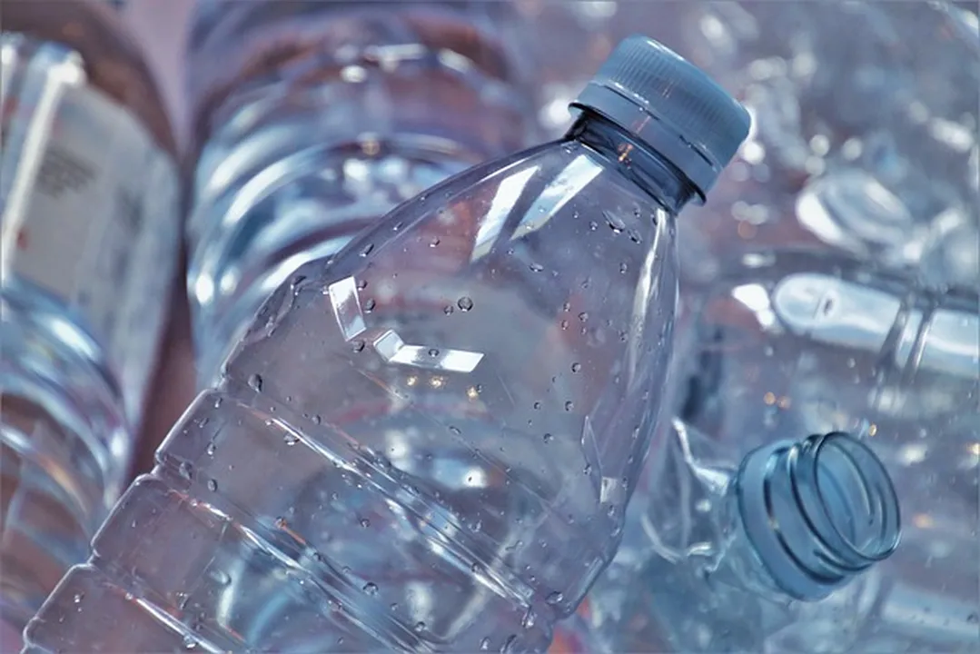 Muestra a una persona depositando botellas de plástico en un contenedor de reciclaje con una sonrisa 