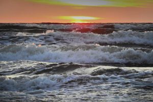 Mar y olas rompiendo con espuma bajo un atardecer naranja