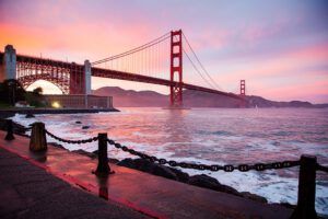 Puente colgante rojo sobre el mar al atardecer junto a la costa que sugiere medidas mitigar acidificacion oceanica