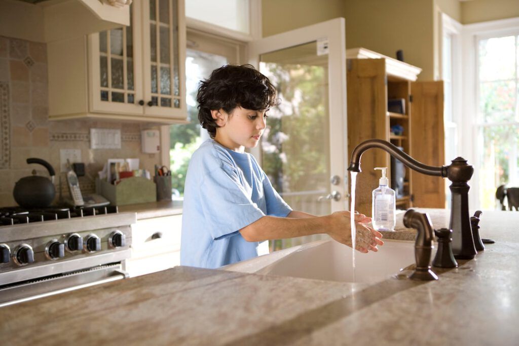 Niño lavándose las manos en la cocina mostrando prácticas de higiene como medidas prevenir especies invasoras