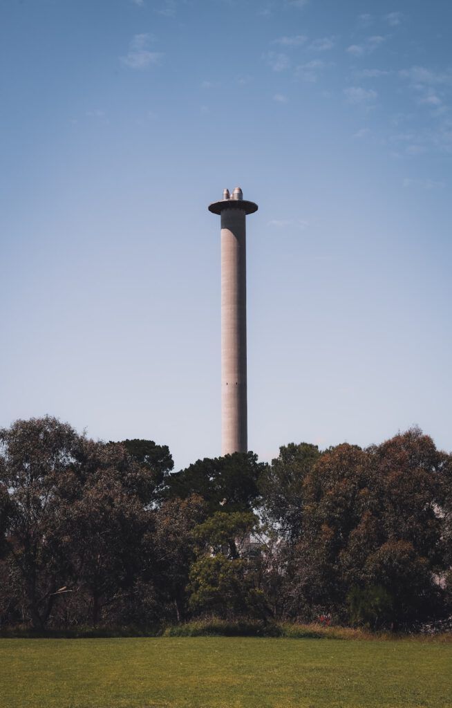 Torre tipo chimenea entre árboles y césped que ilustra medidas reducir contaminacion aire casa mediante control de fuentes y ventilación