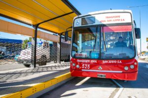 Autobús urbano rojo detenido junto a una marquesina amarilla que ilustra la multimodalidad 1