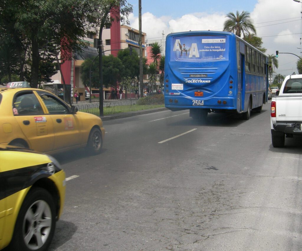 Autobús azul y taxis amarillos en una avenida urbana mostrando emisiones que evocan una noche contaminada.