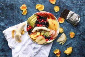 Bowl de frutas frescas con banana, manzana, bayas y chocolate ilustrando prevencion enfermedades estilo vida descubre como hacerlo