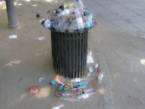 Contenedor de basura público desbordado con botellas de plástico y residuos, reciclaje 4 visible en acciones urbanas