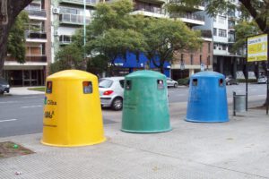 Tres contenedores urbanos de colores en la acera para reciclaje de plasticos en una avenida