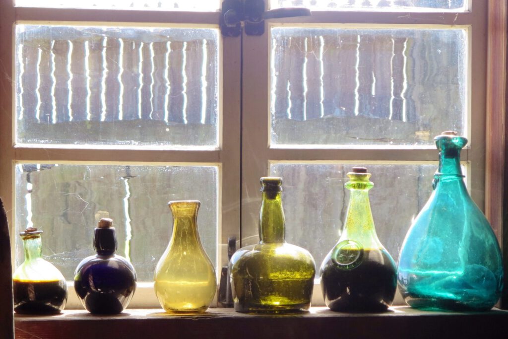 Botellas de colores alineadas en un alféizar iluminado que evocan reciclaje de vidrio