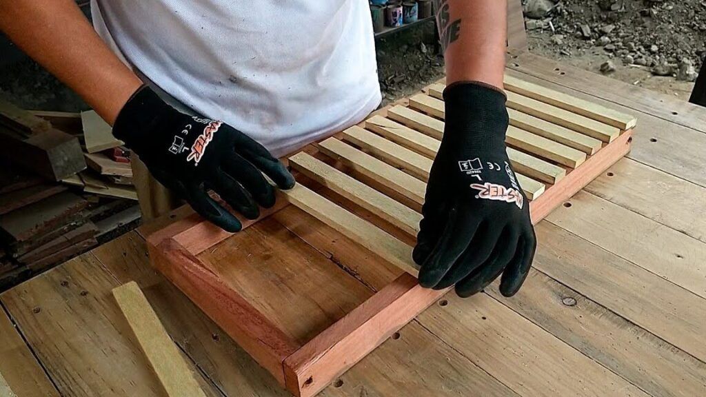 Manos con guantes ensamblando listones de madera en un marco para reciclaje madera.