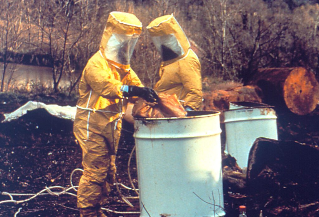 Dos operarios con trajes protectores depositando material en barriles como parte de residuos peligrosos 1